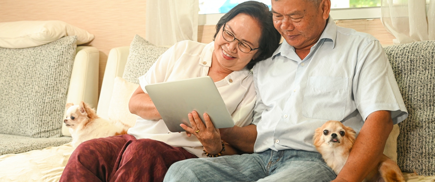 Elderly woman and an asian man sitting on a sofa are using a tablet.
